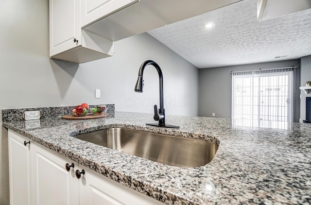 kitchen with light stone counters, white cabinetry, a sink, a textured ceiling, and a peninsula