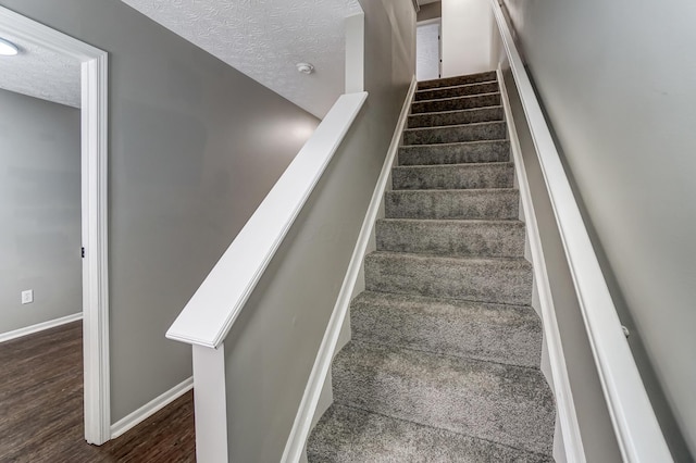 stairs with a textured ceiling, wood finished floors, and baseboards