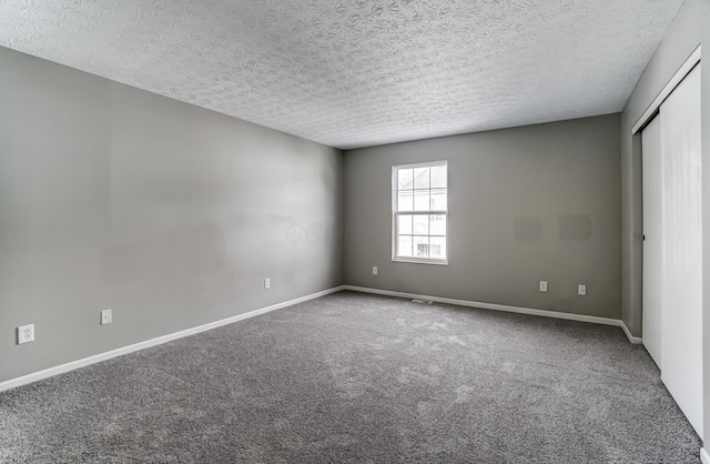 empty room featuring carpet flooring, a textured ceiling, and baseboards