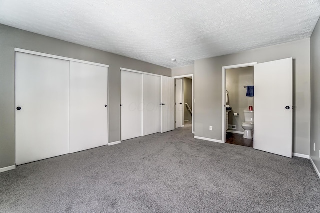 unfurnished bedroom with a textured ceiling, connected bathroom, carpet floors, baseboards, and two closets