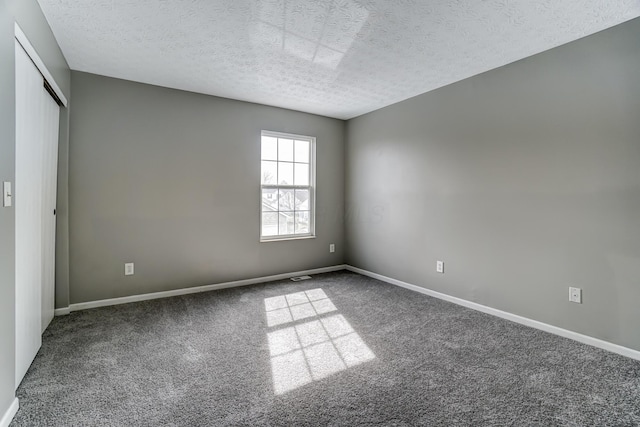 carpeted empty room with a textured ceiling, visible vents, and baseboards