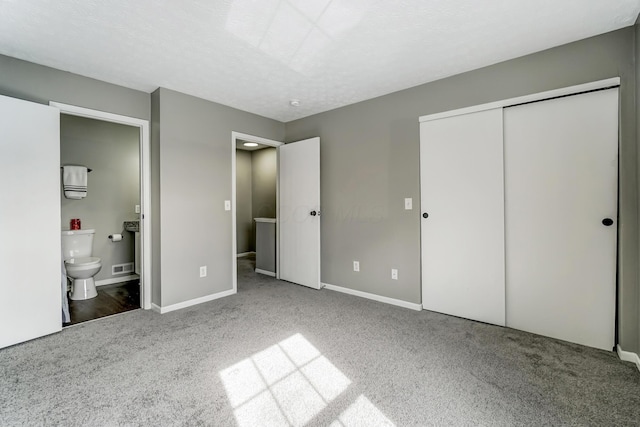 unfurnished bedroom featuring baseboards, ensuite bathroom, a textured ceiling, carpet floors, and a closet