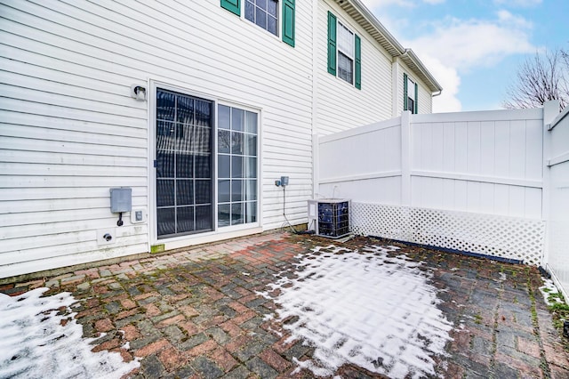 snow covered patio with cooling unit and fence