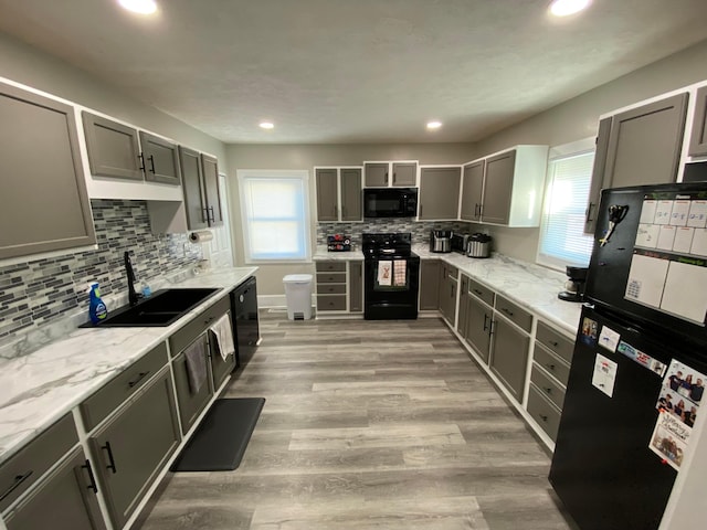 kitchen featuring light wood finished floors, plenty of natural light, gray cabinets, black appliances, and a sink