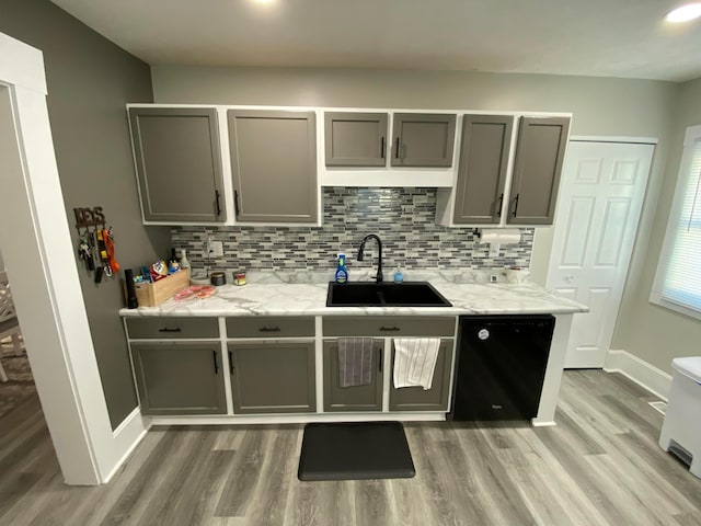 kitchen featuring light wood finished floors, dishwasher, backsplash, gray cabinets, and a sink