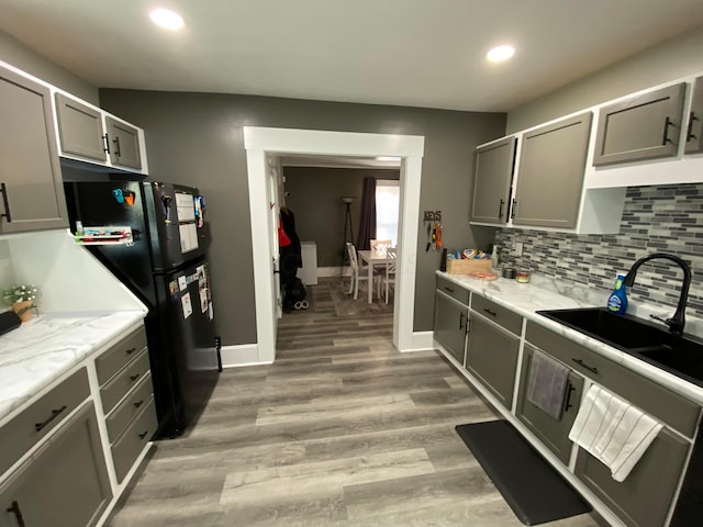 kitchen featuring a sink, light wood-type flooring, gray cabinets, freestanding refrigerator, and tasteful backsplash