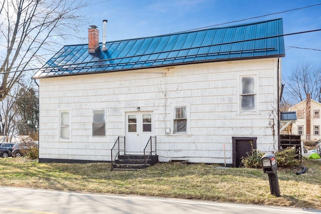 view of front of property featuring entry steps, a chimney, metal roof, a standing seam roof, and a front lawn