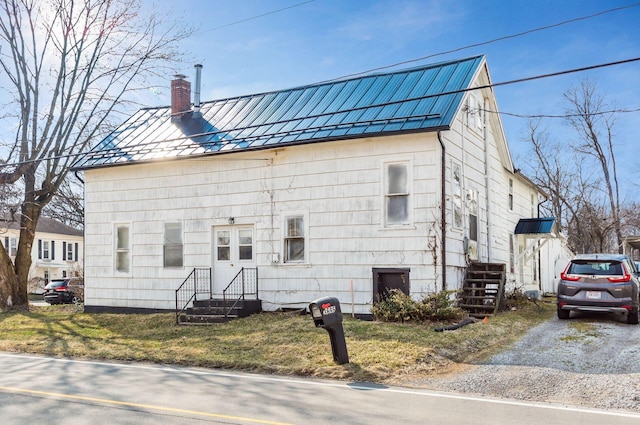 view of front of property with metal roof, a standing seam roof, a chimney, and driveway