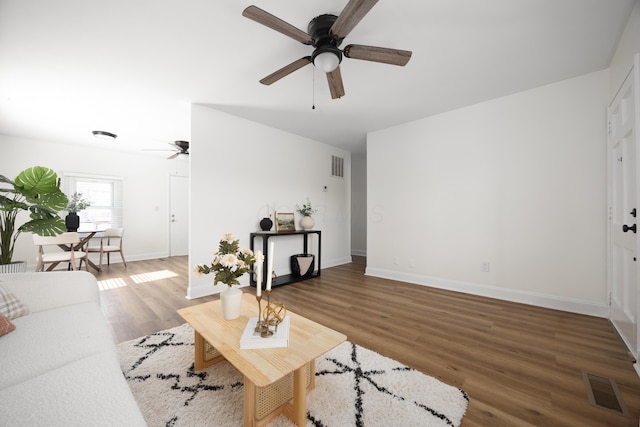 living area featuring dark wood-style floors, visible vents, baseboards, and a ceiling fan