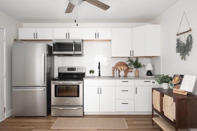 kitchen with dark wood-type flooring, appliances with stainless steel finishes, white cabinets, and a sink