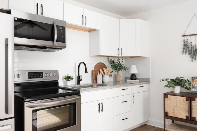 kitchen featuring light stone counters, stainless steel appliances, a sink, white cabinets, and decorative backsplash