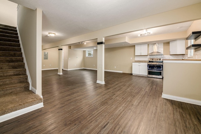 interior space with white cabinets, range with two ovens, open floor plan, dark wood-type flooring, and wall chimney range hood