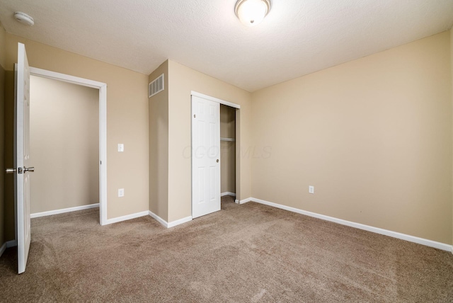 unfurnished bedroom featuring baseboards, visible vents, a textured ceiling, carpet flooring, and a closet