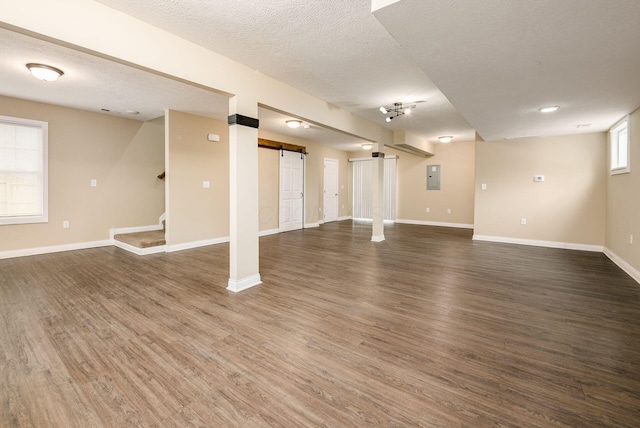 below grade area featuring a textured ceiling, a barn door, dark wood-type flooring, and baseboards