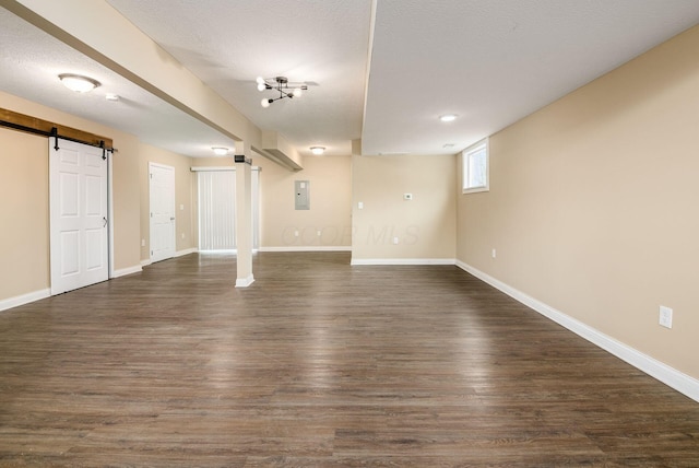 basement with dark wood-style floors, a barn door, electric panel, and baseboards