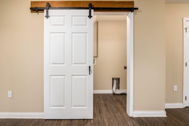 spare room with a barn door, dark wood-style flooring, and baseboards