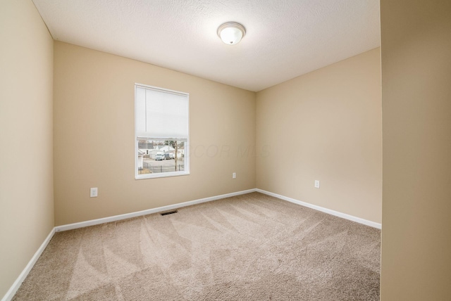 empty room with carpet floors, visible vents, a textured ceiling, and baseboards