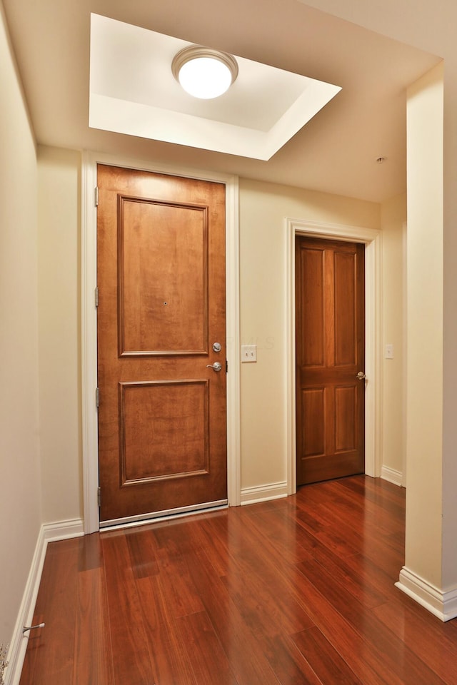 interior space featuring a tray ceiling, dark wood-style flooring, and baseboards