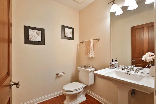 half bathroom featuring toilet, baseboards, a sink, and wood finished floors