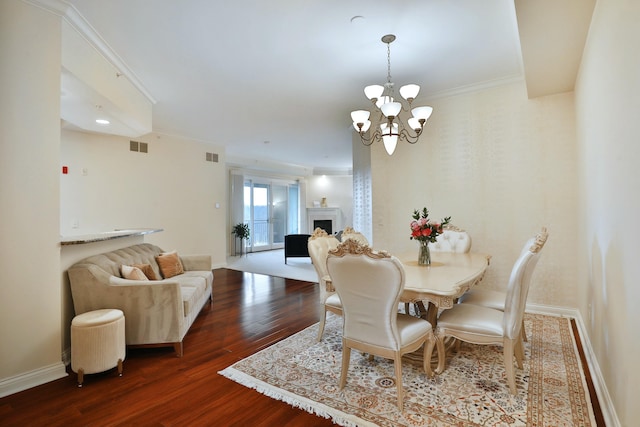 dining area featuring a chandelier, a fireplace, wood finished floors, baseboards, and ornamental molding