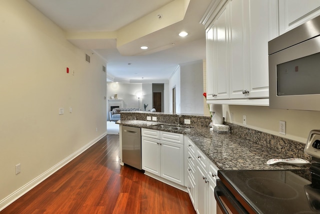 kitchen featuring stainless steel appliances, dark wood-type flooring, open floor plan, a sink, and a peninsula