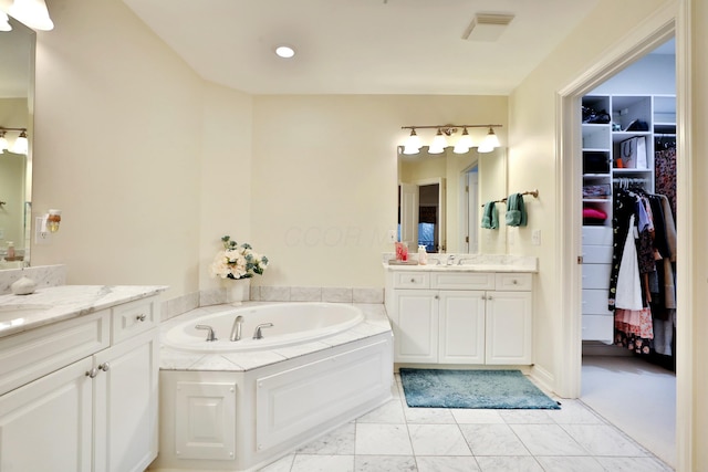 full bathroom with a sink, two vanities, a walk in closet, and a bath