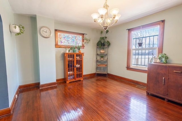 spare room with baseboards, visible vents, hardwood / wood-style floors, and an inviting chandelier