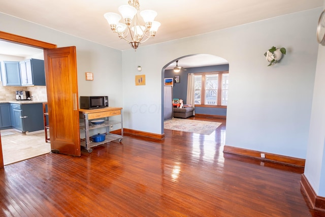 dining room featuring arched walkways, baseboards, a notable chandelier, and hardwood / wood-style floors