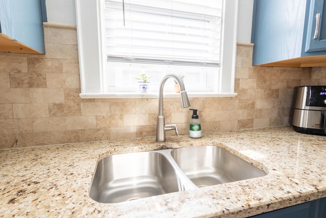 interior details with blue cabinetry, backsplash, a sink, and light stone countertops