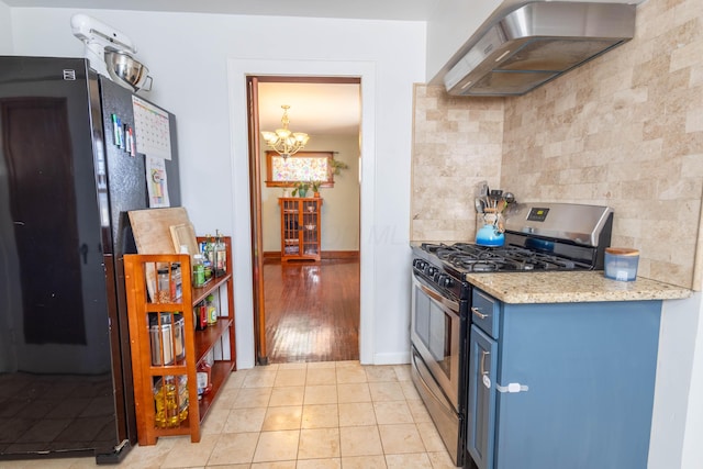 kitchen featuring decorative backsplash, freestanding refrigerator, blue cabinetry, wall chimney range hood, and gas stove