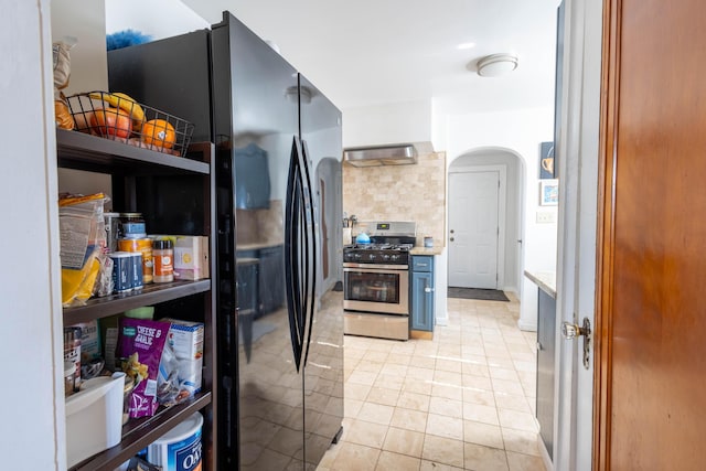 kitchen featuring arched walkways, light tile patterned floors, freestanding refrigerator, stainless steel gas range, and under cabinet range hood