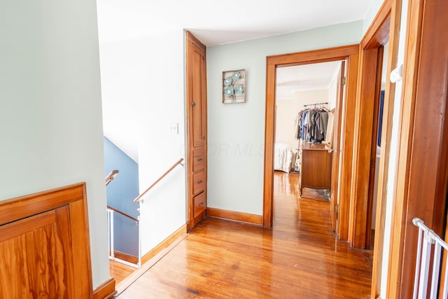 hall featuring light wood-type flooring, an upstairs landing, and baseboards