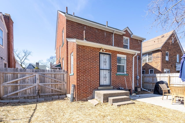 back of house with a gate, fence, a patio, and brick siding