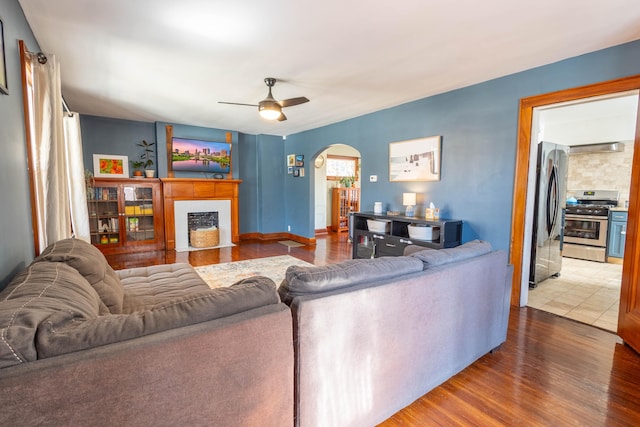 living room with a fireplace with flush hearth, arched walkways, ceiling fan, and wood finished floors