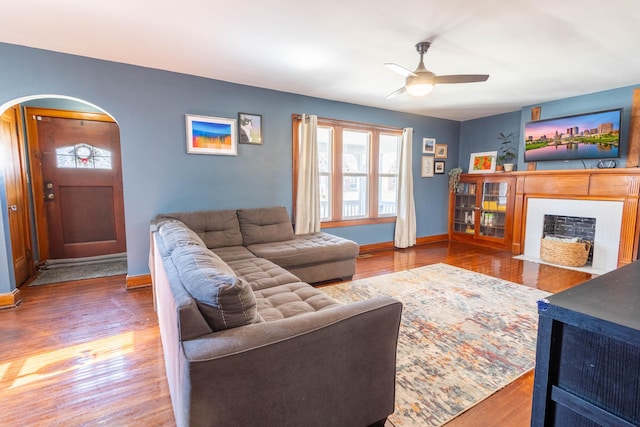 living area featuring arched walkways, a tiled fireplace, wood finished floors, and baseboards