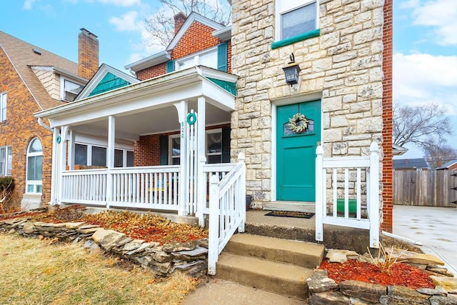 property entrance with stone siding, a porch, and brick siding