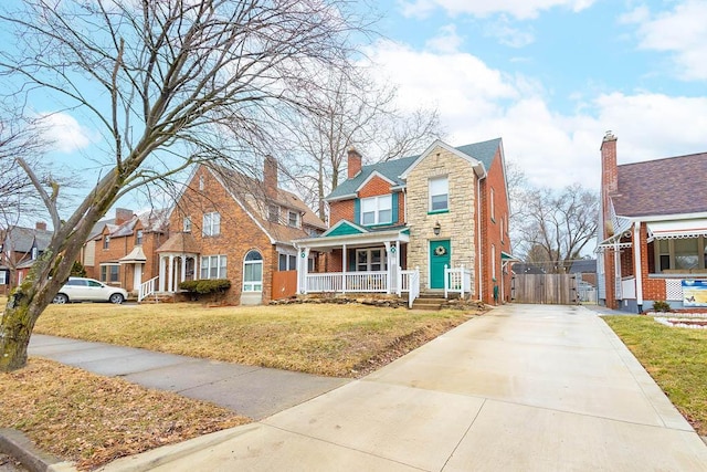 view of front of property featuring covered porch, stone siding, brick siding, and a front yard