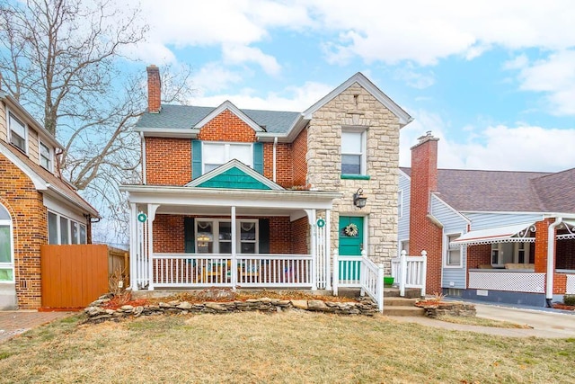 traditional-style home with brick siding, stone siding, a chimney, a porch, and a front yard