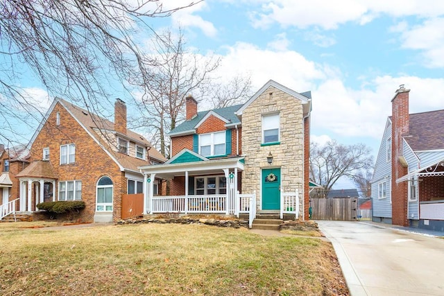 view of front facade with driveway, stone siding, covered porch, a front lawn, and brick siding