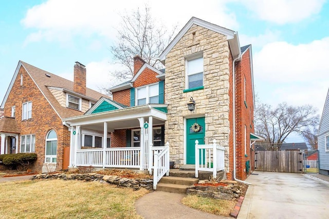 view of front of house with stone siding, fence, a porch, and brick siding