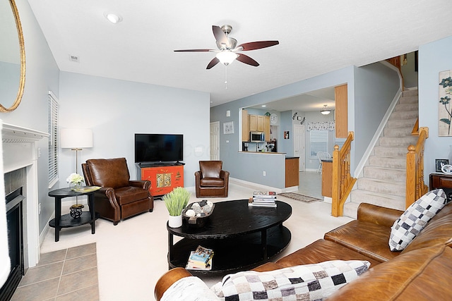 living room with ceiling fan, a fireplace with flush hearth, visible vents, baseboards, and stairs