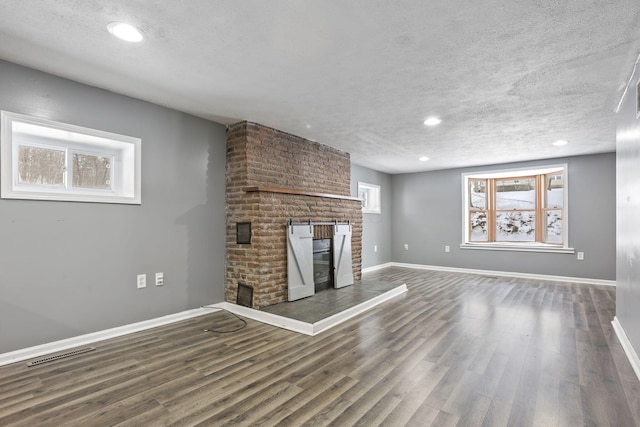 unfurnished living room with a textured ceiling, wood finished floors, visible vents, baseboards, and a brick fireplace