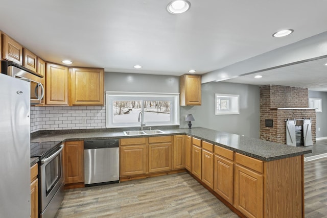 kitchen with stainless steel appliances, dark countertops, a sink, light wood-type flooring, and a peninsula