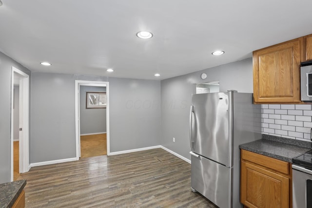 kitchen with stainless steel appliances, dark wood-style flooring, dark countertops, and backsplash