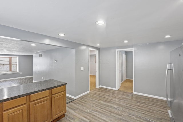 kitchen with recessed lighting, baseboards, freestanding refrigerator, light wood finished floors, and dark countertops