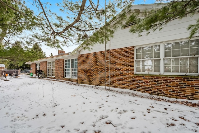 snow covered property featuring brick siding and a chimney