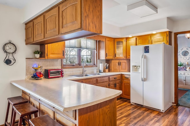 kitchen with a breakfast bar, white refrigerator with ice dispenser, light countertops, a sink, and a peninsula