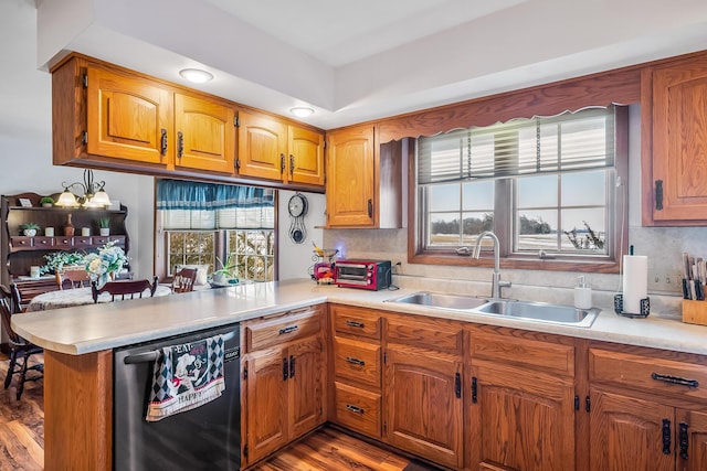 kitchen with brown cabinetry, dishwasher, a peninsula, light countertops, and a sink