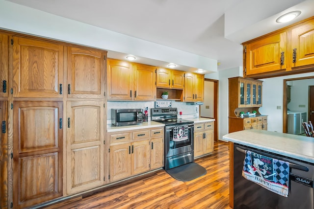 kitchen featuring light wood finished floors, light countertops, backsplash, appliances with stainless steel finishes, and washer and dryer