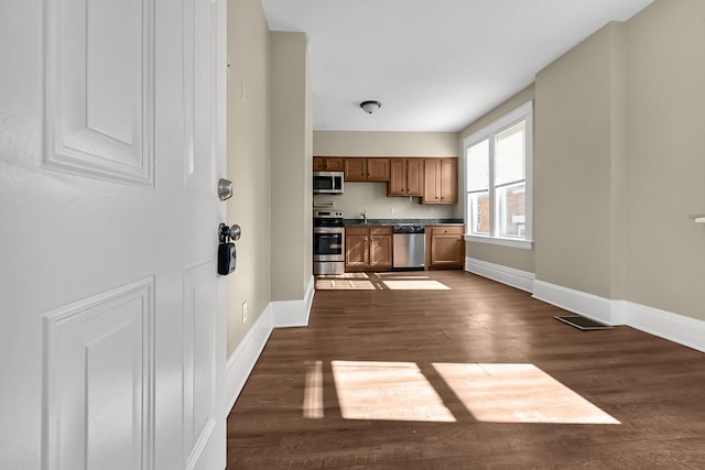 kitchen with baseboards, dark countertops, dark wood-style floors, brown cabinets, and stainless steel appliances